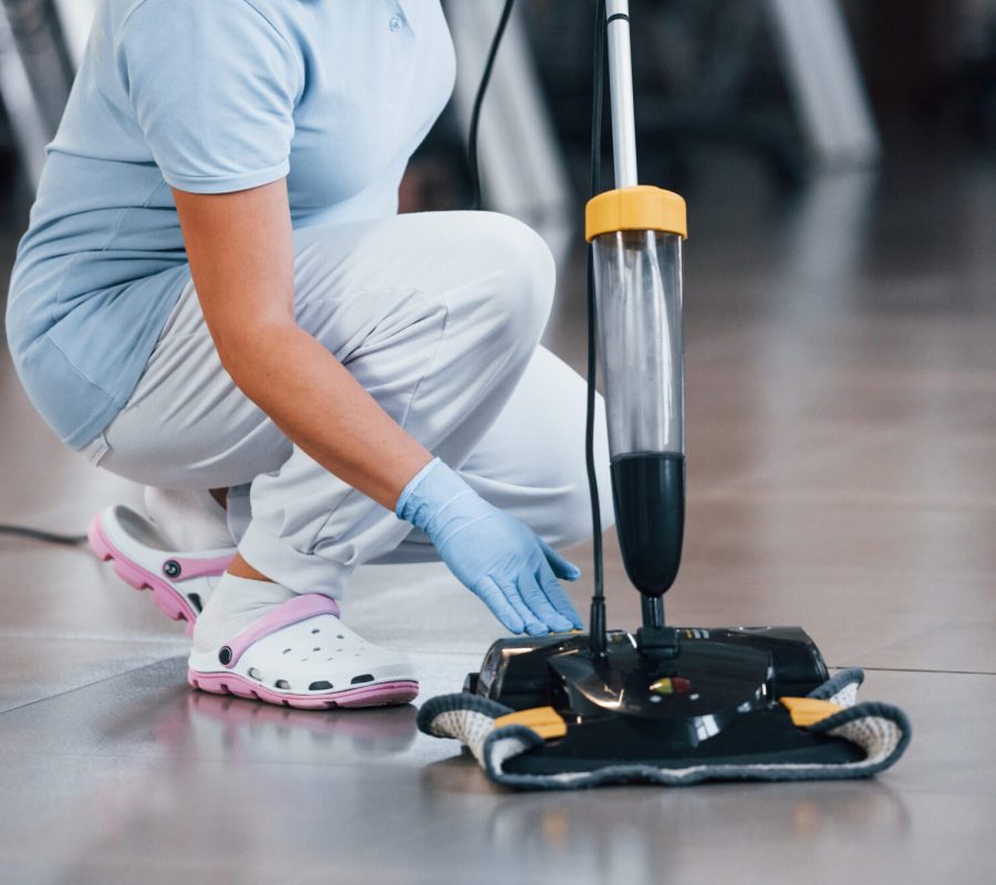 Close up view of woman that uses vacuum cleaner indoor in modern office.
