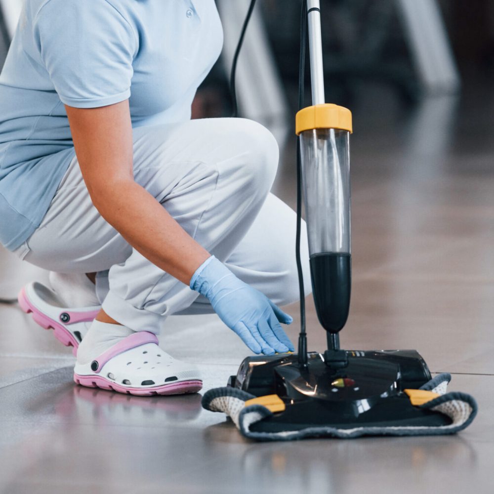 Close up view of woman that uses vacuum cleaner indoor in modern office.